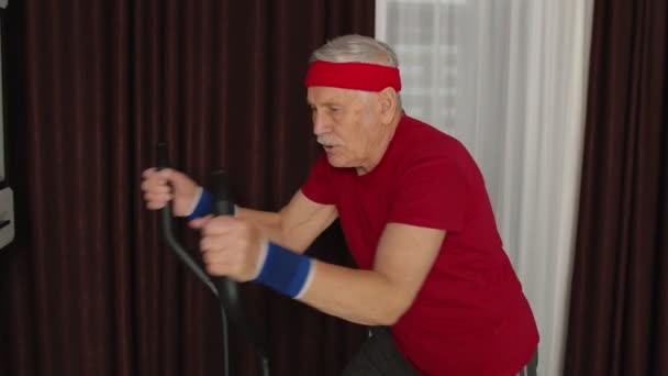Homem sênior usando orbitrek com exercícios de fitness na sala de estar em casa durante o bloqueio do coronavírus — Vídeo de Stock