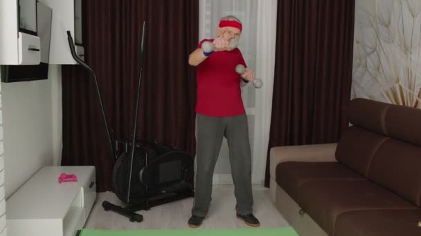 Senior man doet vitaliteit workout gewichtheffen oefeningen met halters thuis tijdens coronavirus — Stockvideo