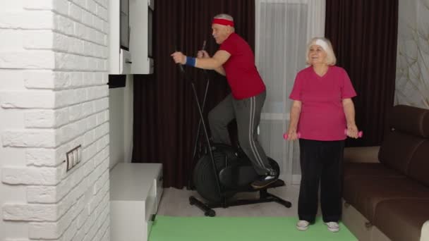 Senior pareja de ancianos usando orbitrek, haciendo ejercicio levantamiento de pesas deporte mancuernas ejercicios en casa — Vídeos de Stock
