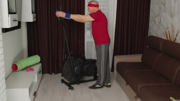 Senior man in sportkleding met behulp van orbitrek in de woonkamer doet sport training cardiotraining thuis — Stockvideo