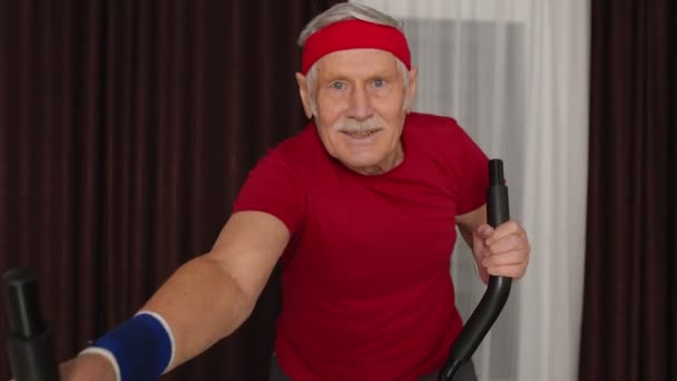 Egészséges idős idős nagypapa modell gyakorló sport edzés orbitrek szobában otthon — Stock videók