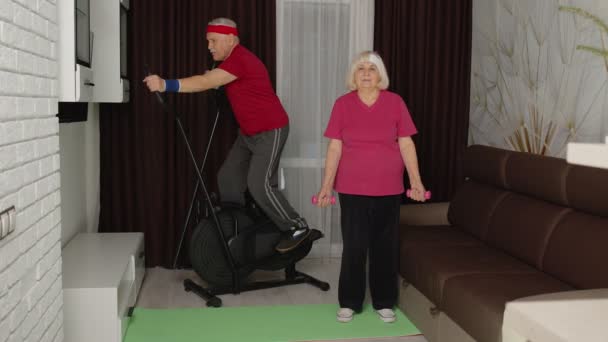 Uomo anziano donna che fa esercizi di sollevamento pesi vitalità manubri sportivi e utilizzando orbitrek a casa — Video Stock