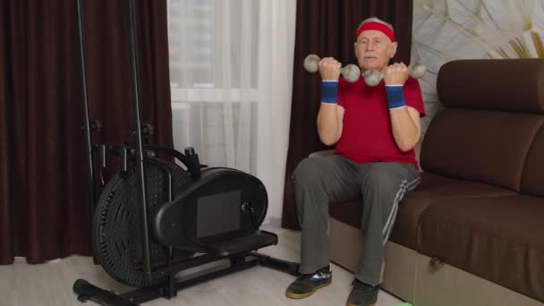 Spor giyim bölümünde yaşlı bir adam ağırlık kaldırıyor. Oturma odasında egzersiz yapıyor. — Stok video