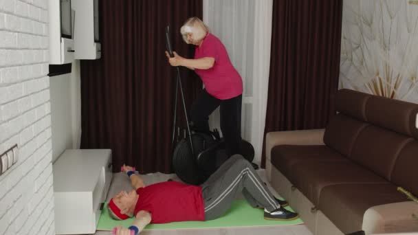 Sénior casal de idosos usando orbitrek, fazendo exercícios de levantamento de peso dumbbells esporte exercícios em casa — Vídeo de Stock