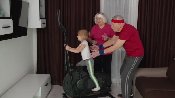 Viejo abuelo activo, abuela entrenamiento nieta niño cómo usar orbitrek en casa — Vídeo de stock