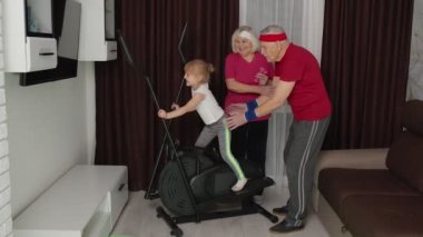 Küçük kız evde orbitrek kullanıyor. Dede ve ninelerle spor antrenmanı yapıyor.