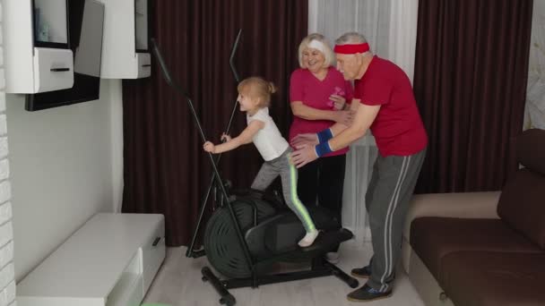 Дитяча дівчина використовує орбітрек вдома займається спортивною підготовкою кардіо вправ з тренерами і бабусями — стокове відео