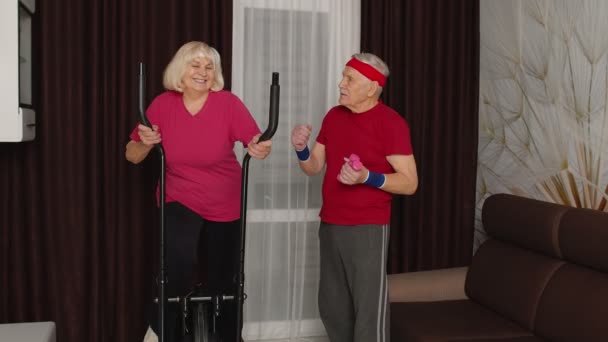 Stara para seniorów ćwiczy na orbitreku, ćwiczy hantle sportowe w domu — Wideo stockowe