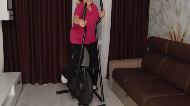 Donna anziana in abbigliamento sportivo con orbitrek ascoltare musica a casa facendo sport cardio esercizi — Video Stock