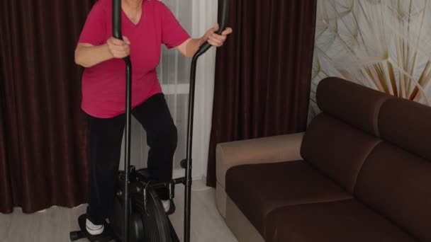 Aktywny zdrowy senior dojrzała kobieta w odzieży sportowej za pomocą orbitrek, trening cardio trening w domu — Wideo stockowe