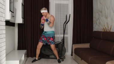 Komik sporcu adam antrenörü. Kol halterleriyle egzersiz yapıyor. Evde internet üzerinden spor yapıyor.