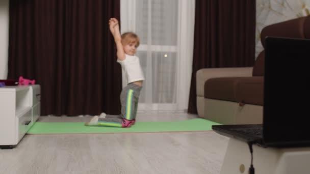 Дівчинка-дівчинка займається гімнастикою розтягування вдома, дивиться онлайн уроки на ноутбук ПК — стокове відео