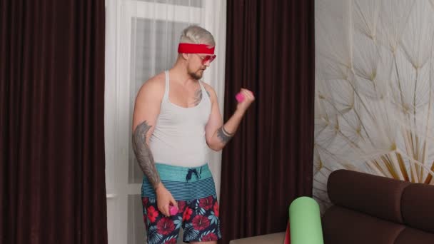 Смешной культурист парень диван показывая бицепсы, спортивная тяжелая атлетика упражнения с гантелями — стоковое видео