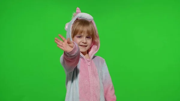 Petite fille enfant souriant, saluant, bonjour ou au revoir avec la main en pyjama licorne sur clé chroma — Photo