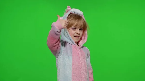 Kleines Mädchen lächelt, zeigt Daumen hoch, unterschreibt im Einhorn-Pyjama auf Chroma-Schlüssel — Stockfoto