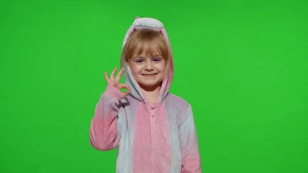 Ragazzina bambina sorridente, mostrando gesto ok, d'accordo segno in pigiama unicorno su sfondo chiave croma — Foto Stock