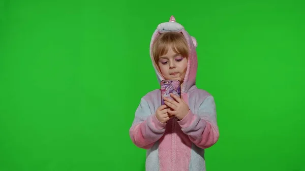 Spännande liten barn flicka i enhörning pyjamas med mobiltelefon, fick reda på stora vinna nyheter — Stockfoto