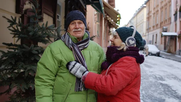 Yaşlı çift, büyükanne, büyükbaba, kışlık ceketli turistler şehirde yürüyor, konuşuyor.