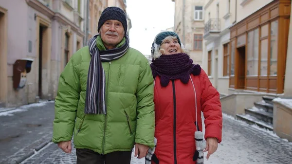 Oudere paar toeristen man vrouw wandelen langs straat in de winter stad, genieten van tijd samen — Stockfoto