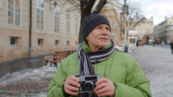 Idős öregember fotózás fényképezőgép, mosolygós segítségével retro eszköz a téli város központjában — Stock Fotó