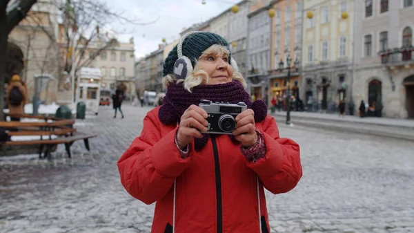 Старшая пожилая женщина турист фотографирует с фотоаппаратом, используя ретро-устройство в зимнем центре города — стоковое фото