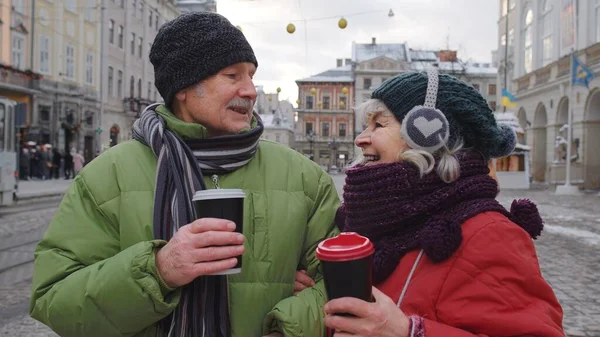 Yaşlı turistler, büyükanne büyükbaba şehir merkezinde yürür, sıcak bir içecek içer, sıcak bir şarap içer.