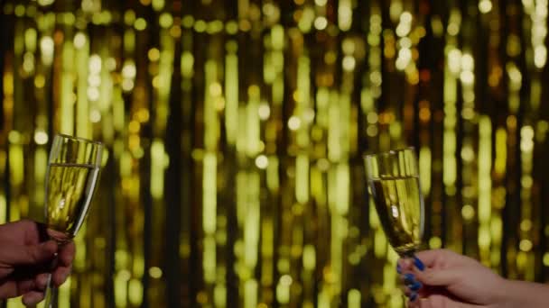 Две руки с бокалами шампанского вина или коктейля, чтобы поднять тост на золотом фоне — стоковое видео
