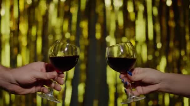 Twee handen met een glas rode wijn maken gejuich, toast heffen op gouden achtergrond in slow motion — Stockvideo
