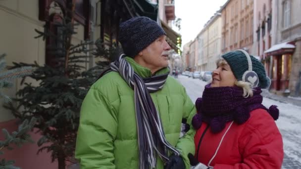 Старші літня пара туристів ходять, обіймаються, цілуються в зимовому місті на канікулах — стокове відео