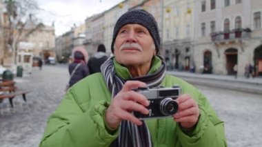 Büyük mutlu büyükbaba fotoğraf makinesiyle fotoğraf çekiyor, açık havada retro cihazıyla gülümsüyor.