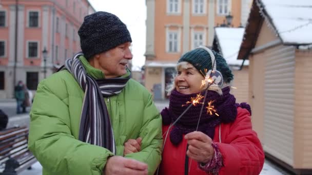 Пожилая семья, держащая бенгальские огни наслаждаясь канун Рождества, отмечая день рождения на городской улице — стоковое видео
