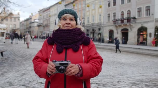 Старша жінка-туристка фотографує з фотоапаратом, використовуючи ретро пристрій в зимовому місті, блокування — стокове відео