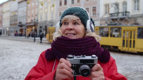 Senior vieja turista tomando fotos con cámara fotográfica, utilizando dispositivo retro en el centro de la ciudad de invierno — Vídeos de Stock