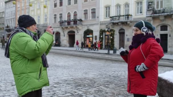 Senior fru poserar för kameran skrattar medan man tar bilder på vintern stad gata — Stockvideo