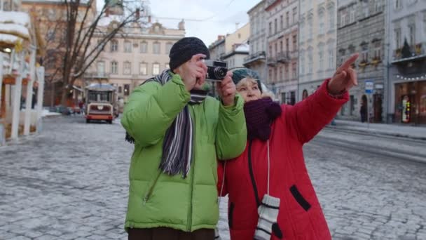 Senior vrouw echtgenoot toeristen het nemen van foto 's op retro camera, wandelen op de winter stad straat — Stockvideo