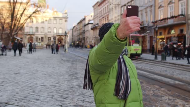 Grand-père touristique âgé voyageant, prenant selfie, faire un appel vidéo en ligne sur le centre-ville d'hiver — Video