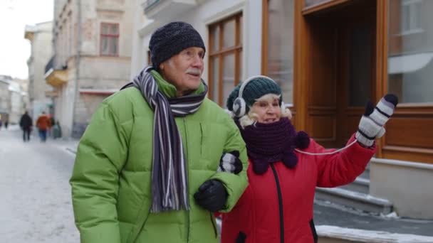 Oudere oude echtpaar grootmoeder en grootvader in kleurrijke winterjassen wandelen in de winter stad — Stockvideo