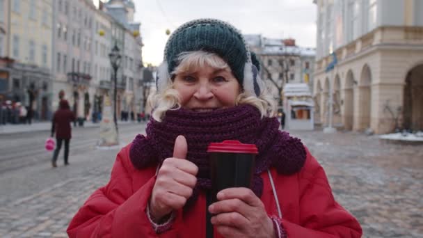 Senior žena babička turista s úsměvem, ukazující palec nahoru v zimě centrum města Lvov, Ukrajina — Stock video
