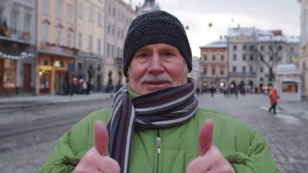 Snygg gammal senior man turist leende, visar tummen upp i vinter centrum av Lviv, Ukraina — Stockvideo