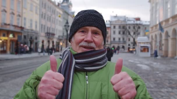 Senior gubbe farfar turist leende, visar tummen upp i vinter centrum av Lviv, Ukraina — Stockvideo