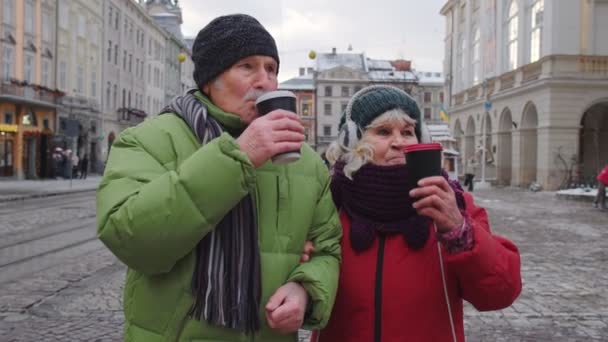 Старшие старые туристы бабушка пешком дедушка, пить горячий напиток глинтвейна в центре города — стоковое видео