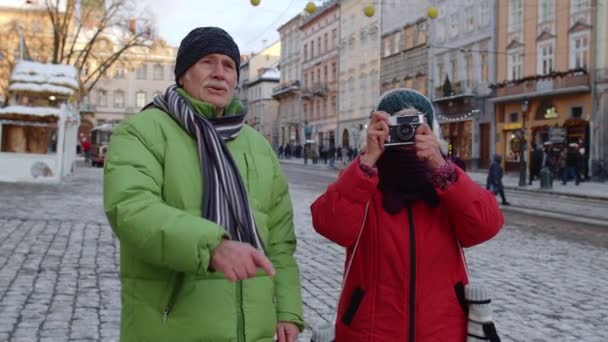 Старшая жена муж туристы, делающие фото на ретро-камеру, прогулки по улице зимнего города — стоковое видео