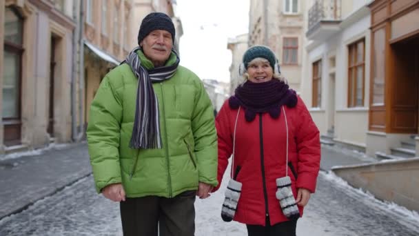 Пожилая пара туристов мужчина женщина семья ходить, говорить, жесты на зимней снежной улице города — стоковое видео