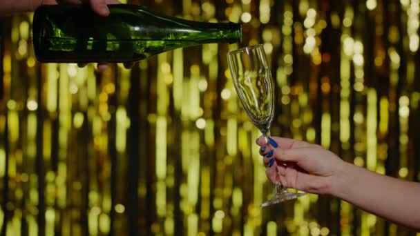 Алкогольный напиток шампанского наливают из бутылки в питьевой стекло золотой фон в замедленной съемке — стоковое видео