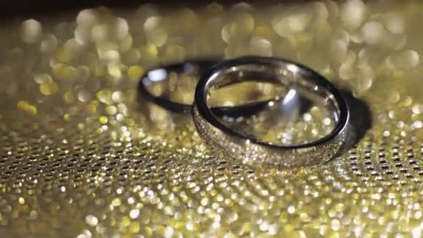 Anillos de boda acostados, giran, giran sobre una superficie brillante dorada brillante con luz, macro de primer plano — Vídeo de stock