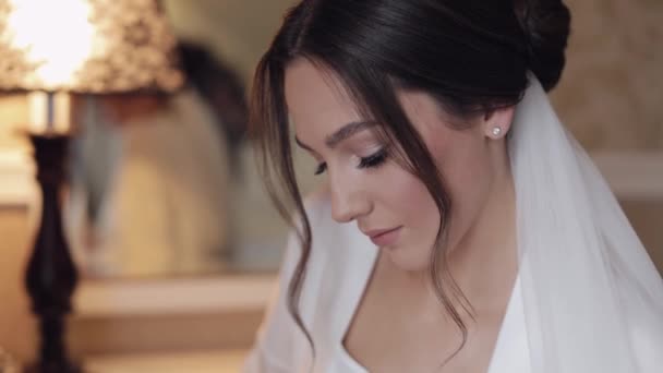 Hermosa novia en vestido de tocador blanco mirando a la cámara y sonriendo, preparativos de la mañana de boda — Vídeos de Stock