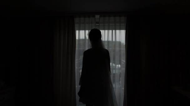 Belle mariée en robe de boudoir blanc va au balcon et ouvre les rideaux dans la chambre d'hôtel ou appartement — Video