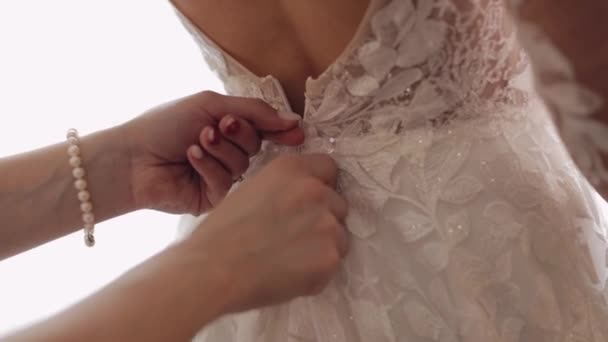 Gravatas de dama de honra e ajuda a colocar o vestido de noiva, preparação matinal da noiva com vestido branco — Vídeo de Stock