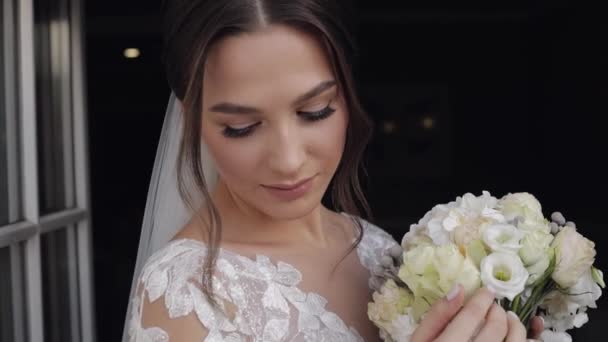 Noiva em vestido de noiva e véu com buquê de flor do noivo ficar perto de portas da varanda em casa — Vídeo de Stock