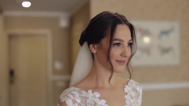 Lovely bride in white wedding dress and veil stay at home in living room, looking at camera, smiling — Stock Video